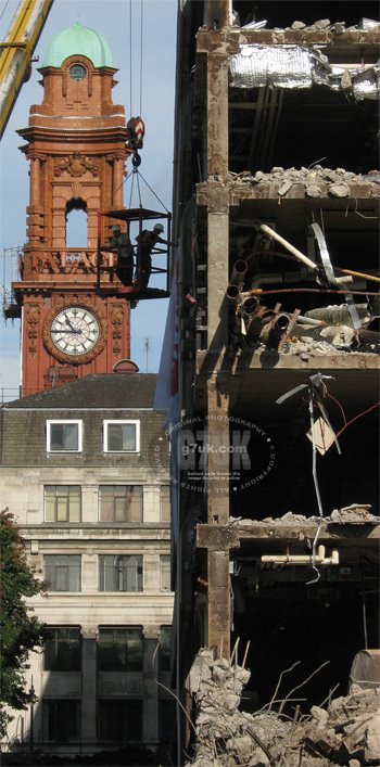 Workmen in a cage suspended from a crane inspect the front of the former BBC building during demolition